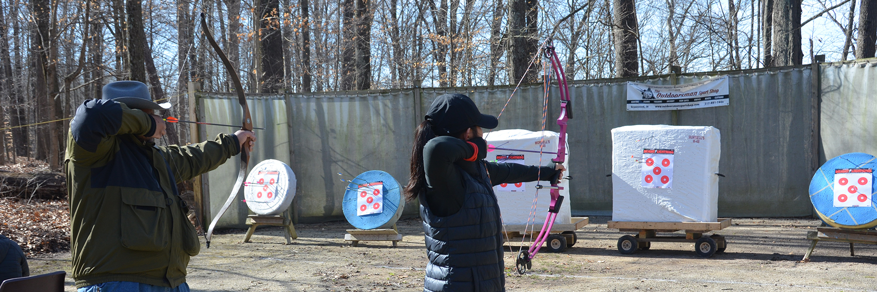 Two staff members in silhouette aiming bows and arrows at archery targets.